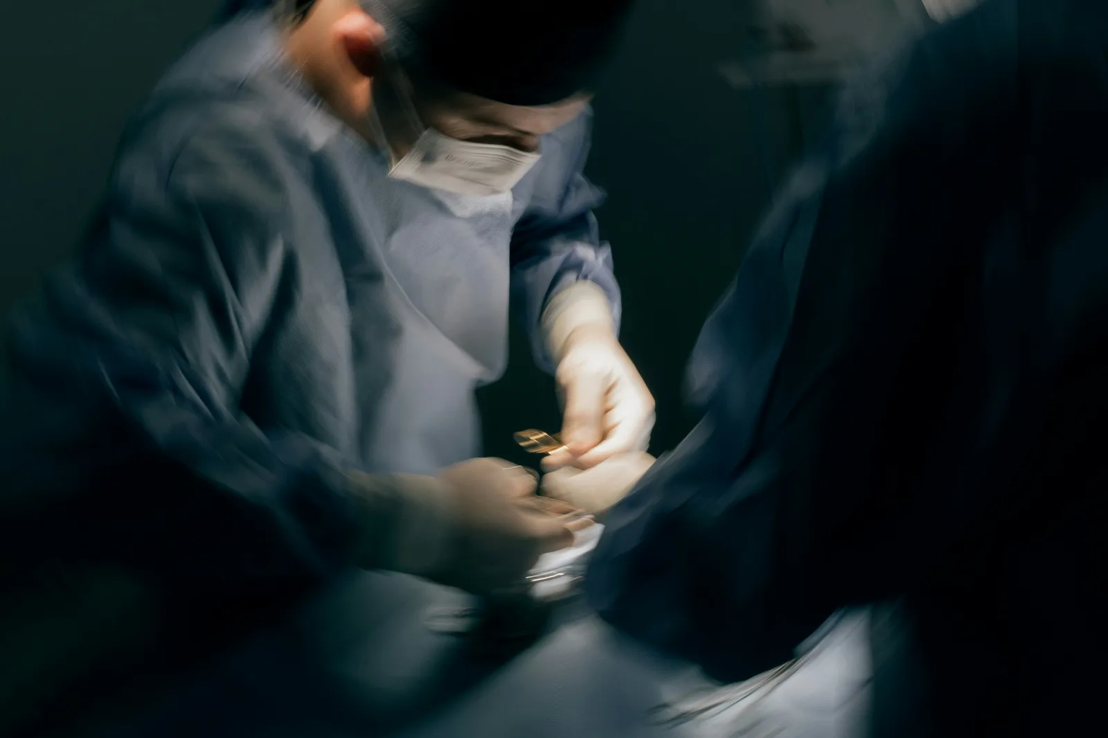 Profissionais de saúde em sala cirúrgica, focados em instrumentos durante procedimento médico complexo.