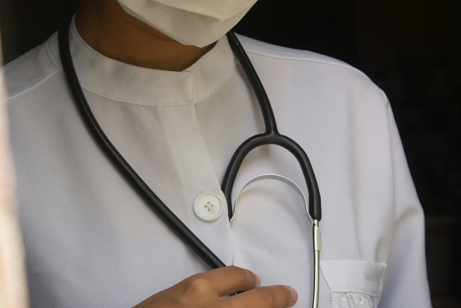 Profissional de saúde com máscara e óculos segura estetoscópio, simbolizando a atenção humana essencial na avaliação de dados sensíveis de pacientes.