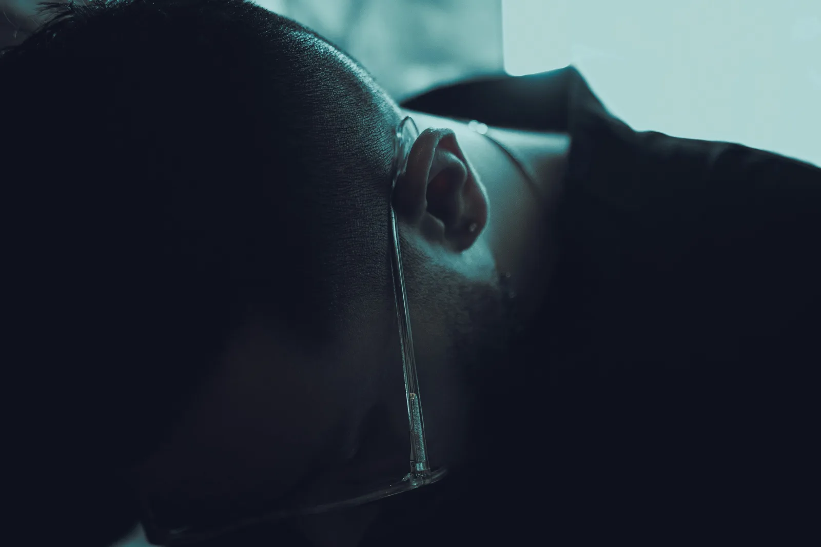Close-up de perfil de uma pessoa em ambiente escuro, iluminada por luz azul, refletindo sobre o agendamento de consultas médicas.
