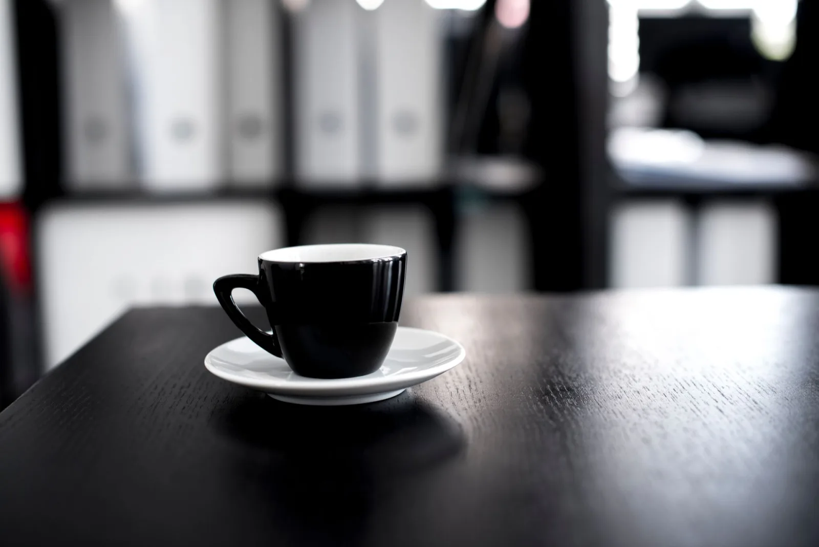 Xícara de café preta em mesa de madeira escura, com fundo de escritório desfocado. Representa a pausa para refletir sobre custos ocultos de IA e LGPD em clínicas.