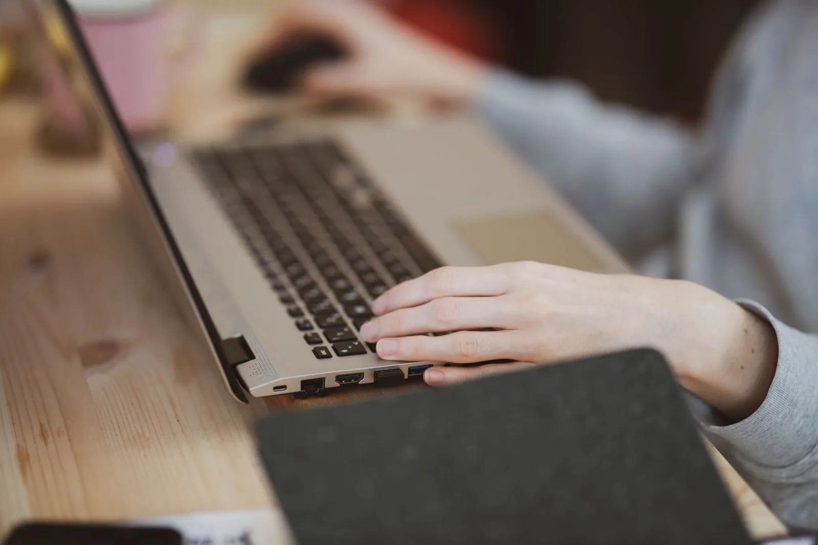 Mãos digitando em um laptop prateado, com foco nas teclas e nas portas laterais do aparelho, simbolizando a segurança de dados em clínicas.