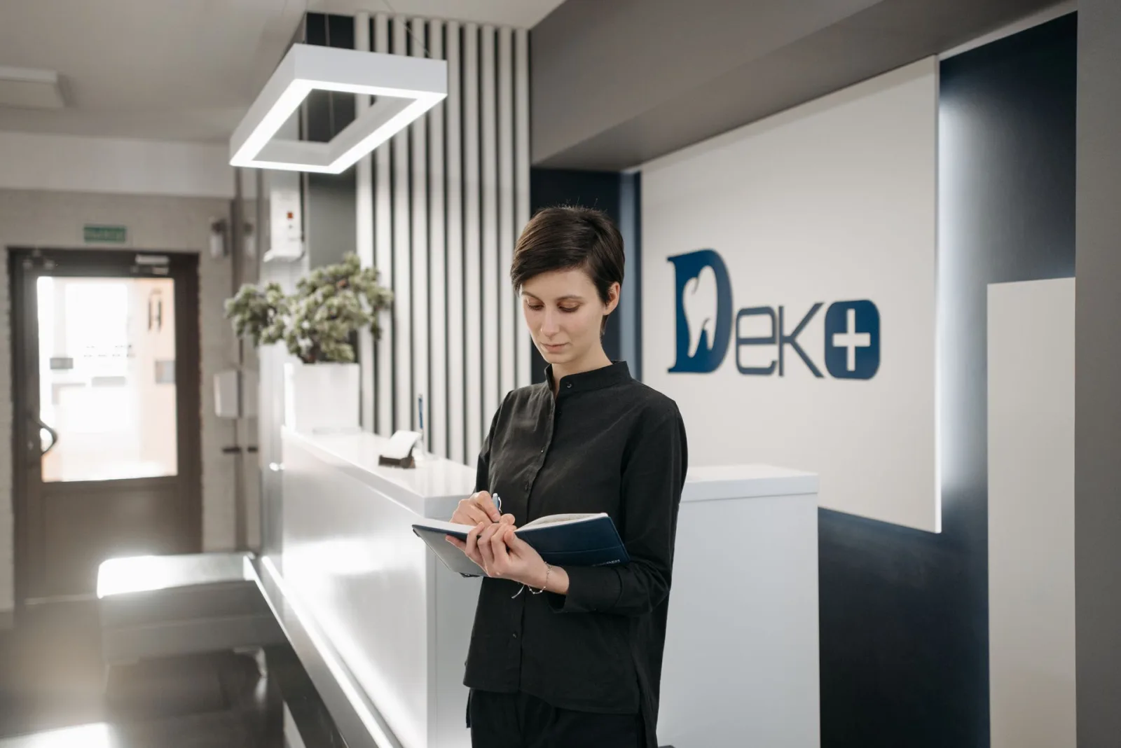 Recepcionista em clínica moderna anota em caderno, representando a gestão de tarefas e processos administrativos.