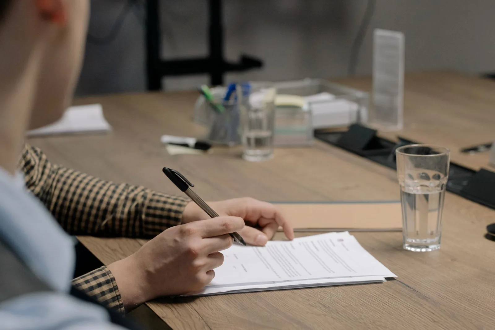 Mão de uma pessoa escrevendo com caneta em um documento sobre uma mesa de madeira, simbolizando revisão e decisão de dados em clínicas.