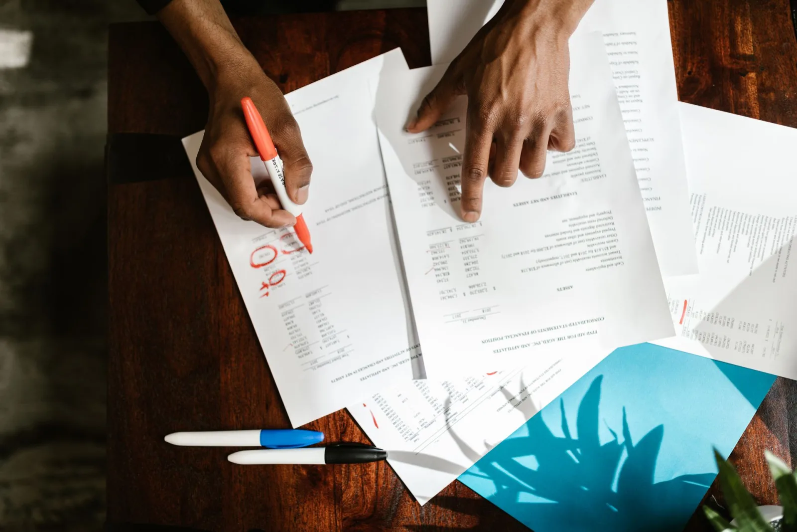 Mãos de gestor de clínica revisando documentos financeiros e fazendo anotações sobre fluxo de caixa e faturamento para gestão eficiente.