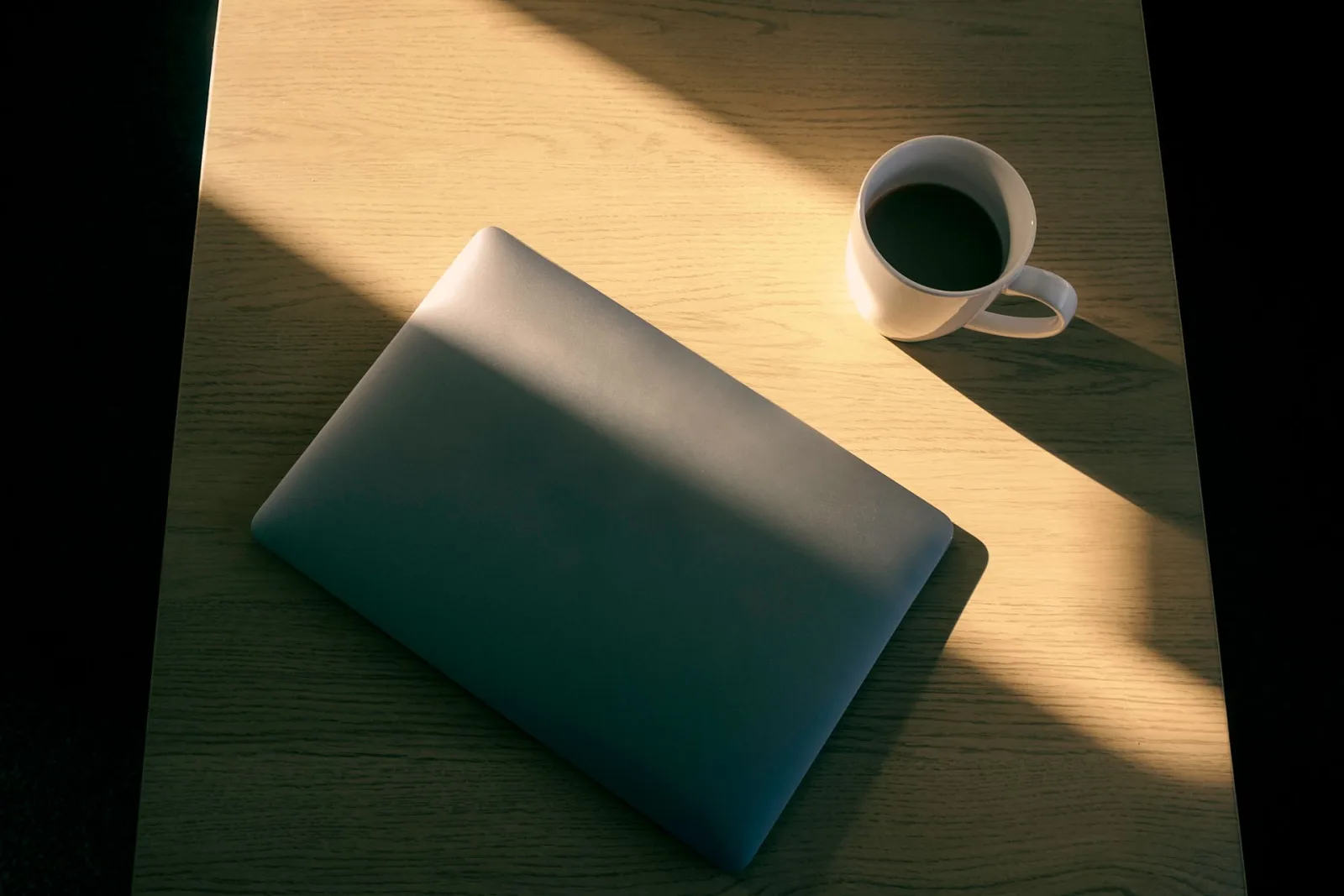 Um notebook aberto e uma xícara de café sobre uma mesa de madeira, banhados por luz natural, simbolizando a reflexão estratégica sobre precificação em clínicas.