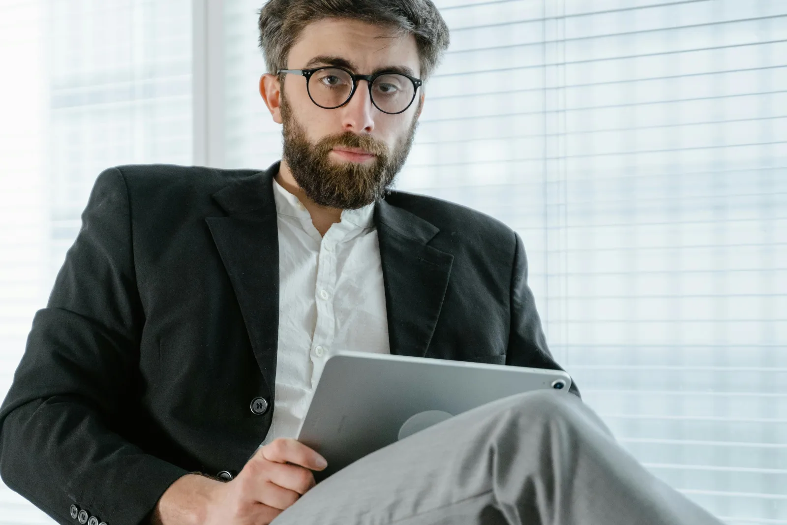 Profissional de saúde com óculos e barba, sentado em escritório, analisando dados em tablet para decisões estratégicas.