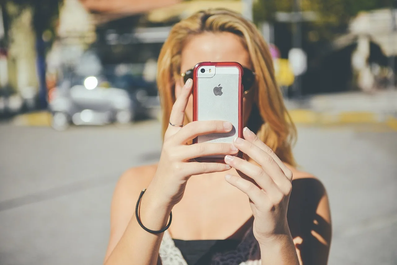 Pessoa loira segura smartphone vermelho cobrindo o rosto, simbolizando privacidade e controle na comunicação digital.