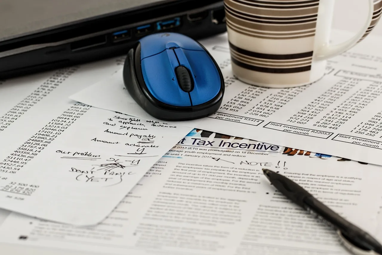 Mesa de trabalho com laptop, papéis com anotações e números, simbolizando planejamento financeiro e gestão estratégica de clínicas.
