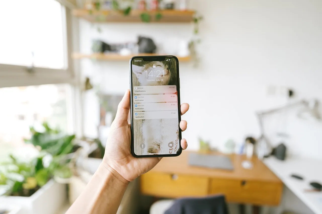 Mão segurando smartphone com tela de bloqueio exibindo hora, data e notificações, representando a interface de chatbots de fluxo fixo em clínicas.