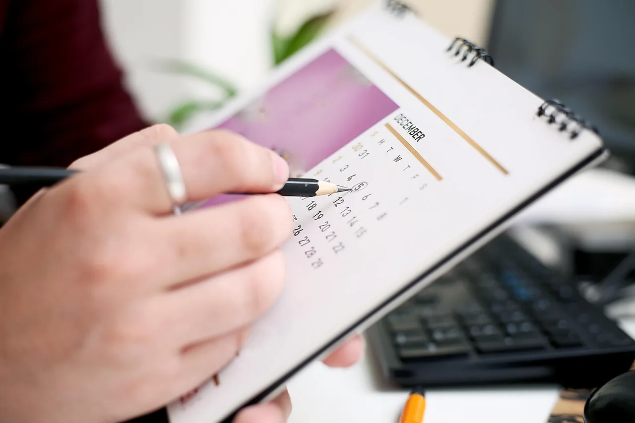 Mão de pessoa marcando a data cinco de dezembro em um calendário de mesa com um lápis, simbolizando organização e planejamento de follow-up de orçamentos em clínicas de saúde.