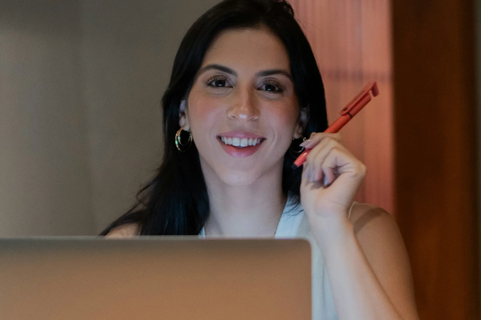 Mulher sorridente com caneta vermelha e laptop, simbolizando produtividade e foco em reuniões de equipe de clínicas.