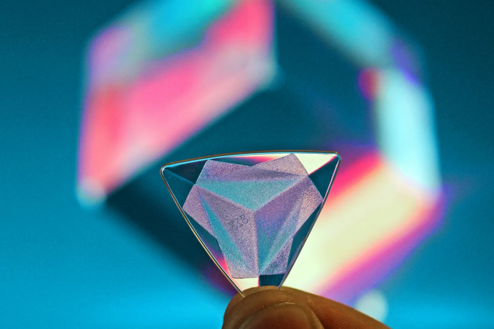 Mão segurando um pequeno cristal triangular contra fundo azul desfocado. Simboliza clareza e foco estratégico para clínicas de saúde.