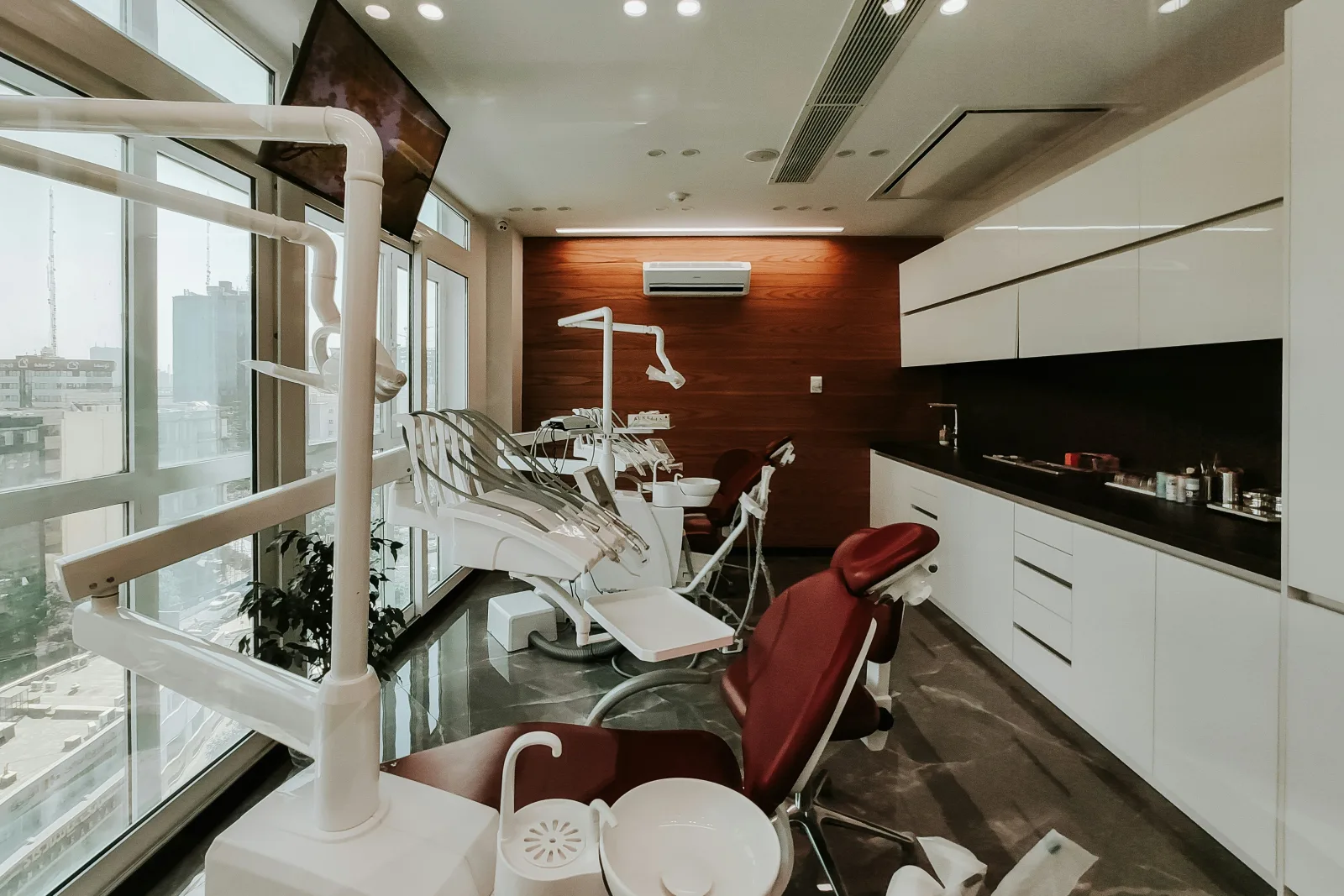 Moderna sala de atendimento odontológico vazia com cadeiras brancas e vermelhas, equipamentos e vista para a cidade, simbolizando horários disponíveis na agenda da clínica.