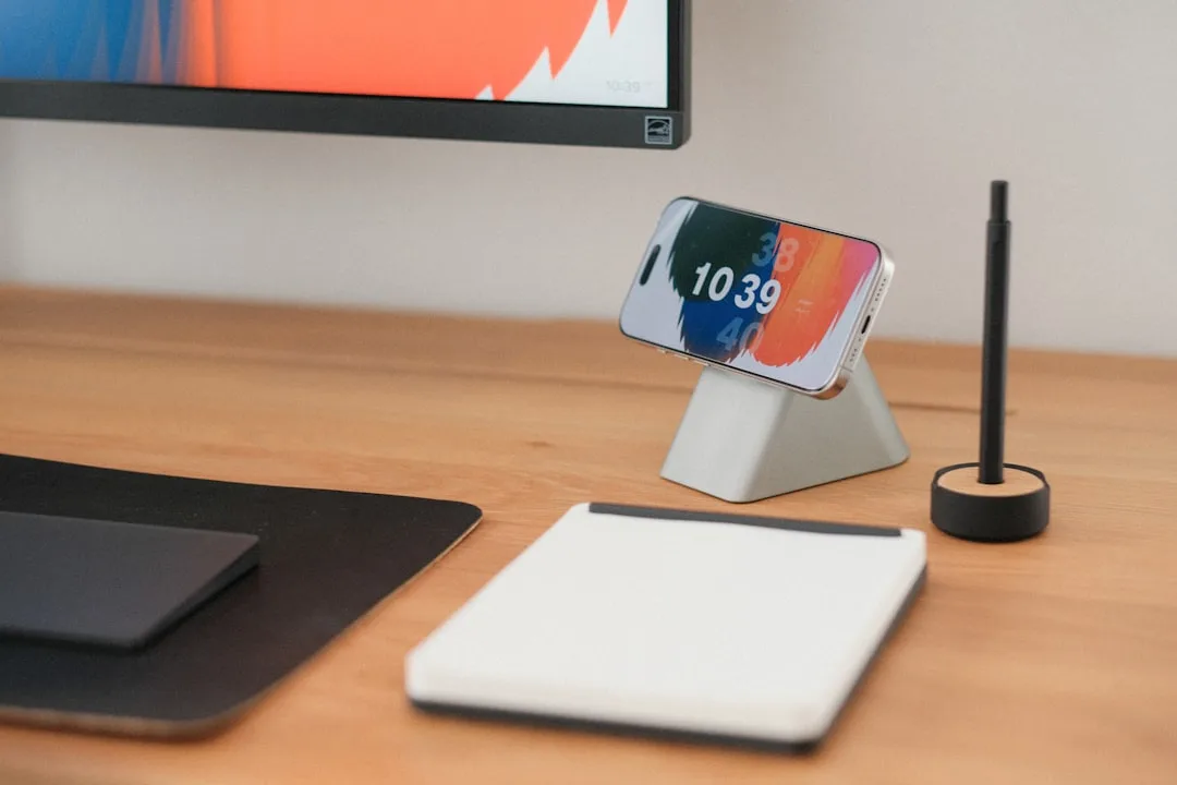 Mesa de madeira organizada com smartphone em suporte, caderno e caneta, simbolizando gestão de dados e planejamento financeiro para clínicas.