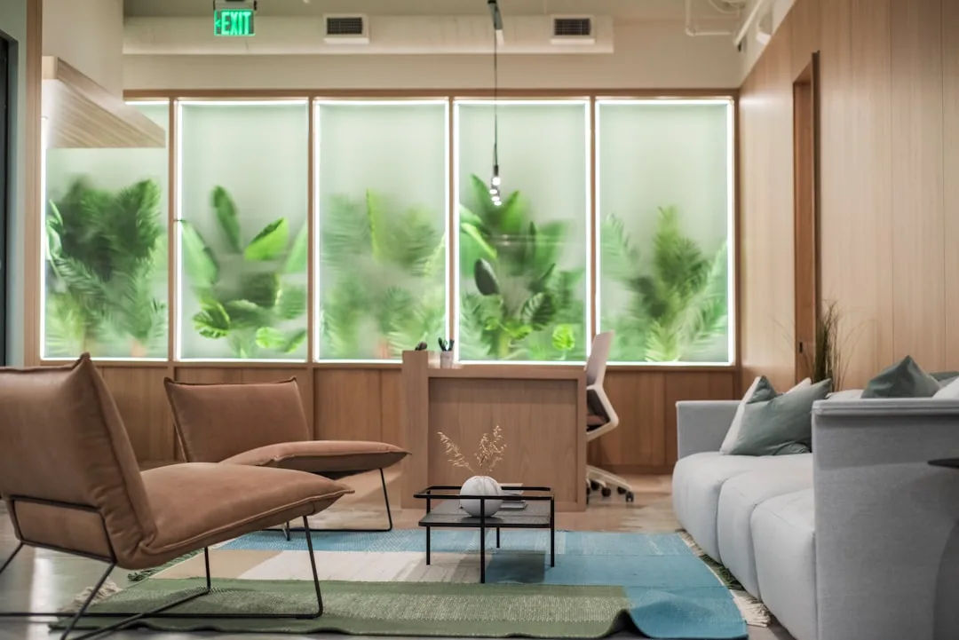 Recepção moderna de clínica de saúde com design acolhedor, paredes de vidro, plantas e mobiliário elegante, transmitindo profissionalismo e bem-estar.